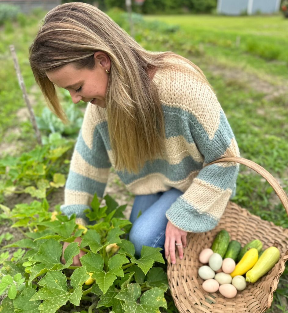 Girl in garden picking squash with gathering basket filled with veggies and eggs.