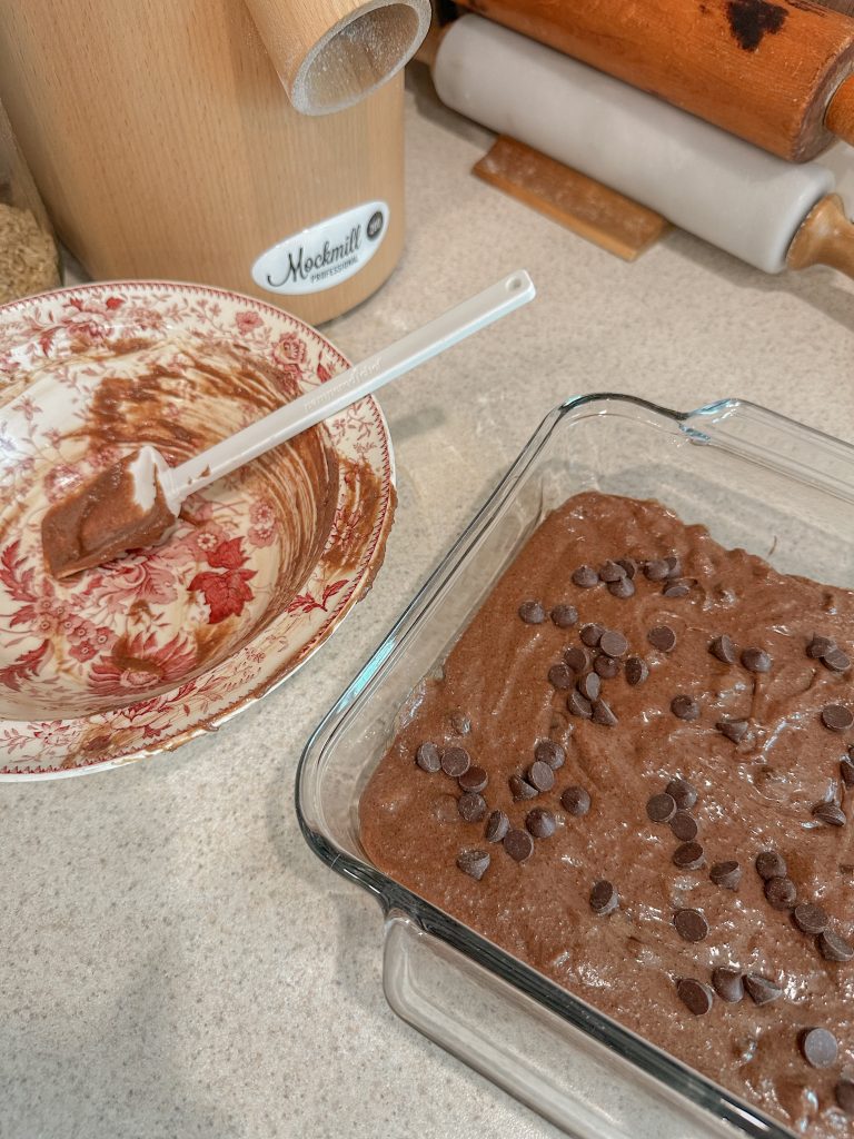 brownie batter in pan ready to bake beside empty pink and white batter bowl on white counter