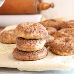 Easy homemade bagels with freshly milled flour setting on parchment paper on kitchen counter beside grain mill and rolling pins