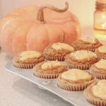 Pumpkin muffins with maple cream cheese in muffin tin setting on counter in front of orange pumpkin and lit candle